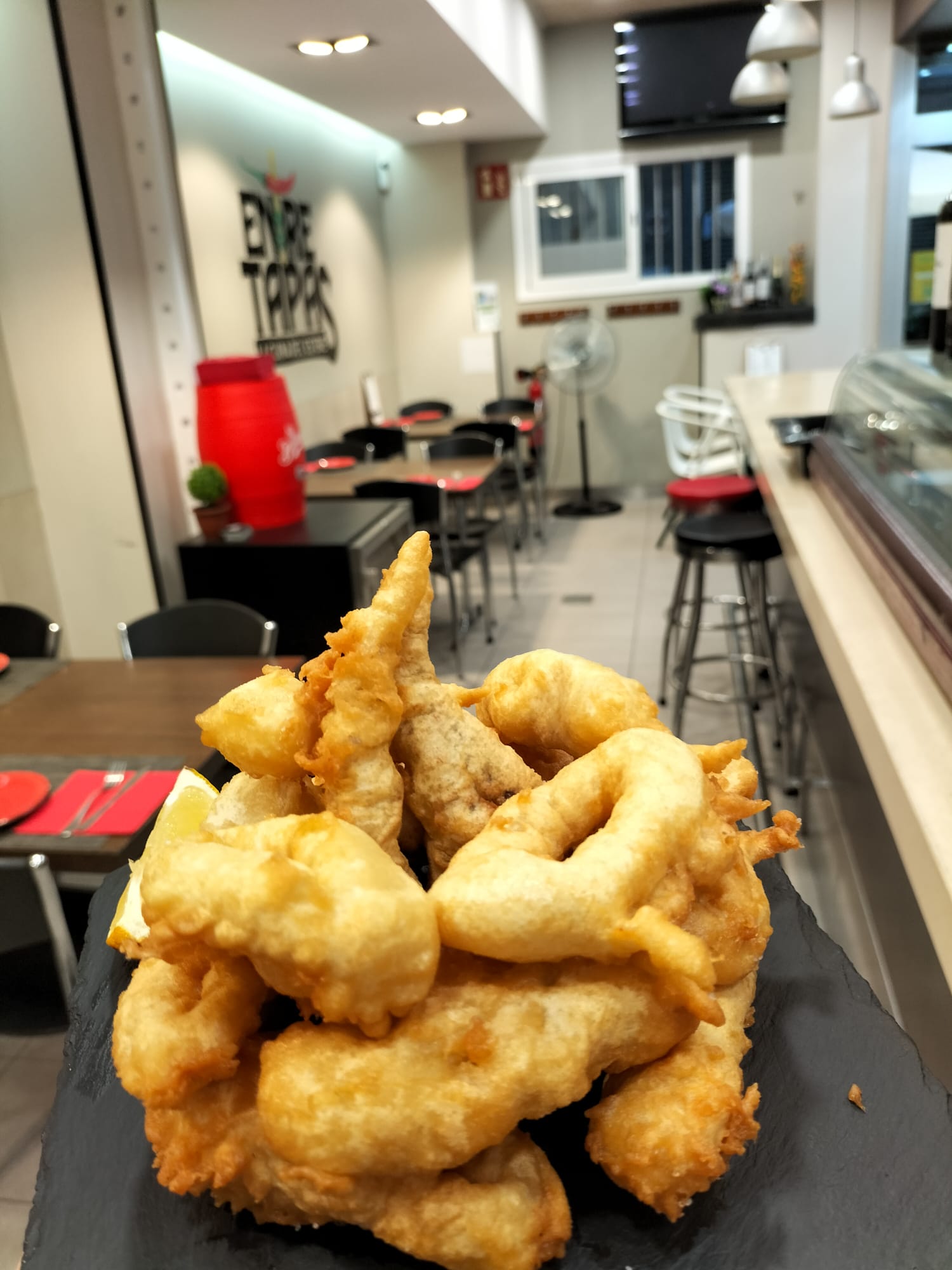Ración de calamares a la andaluza en la barra de Entre Tapas, con el local de fondo