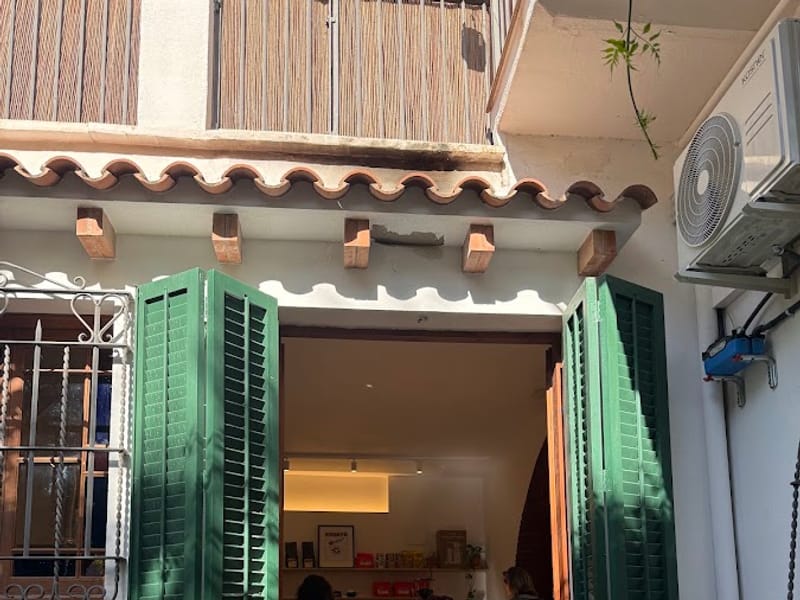 Entrada de KRUSTÔ con contraventanas verdes en la Plaça de la Vila