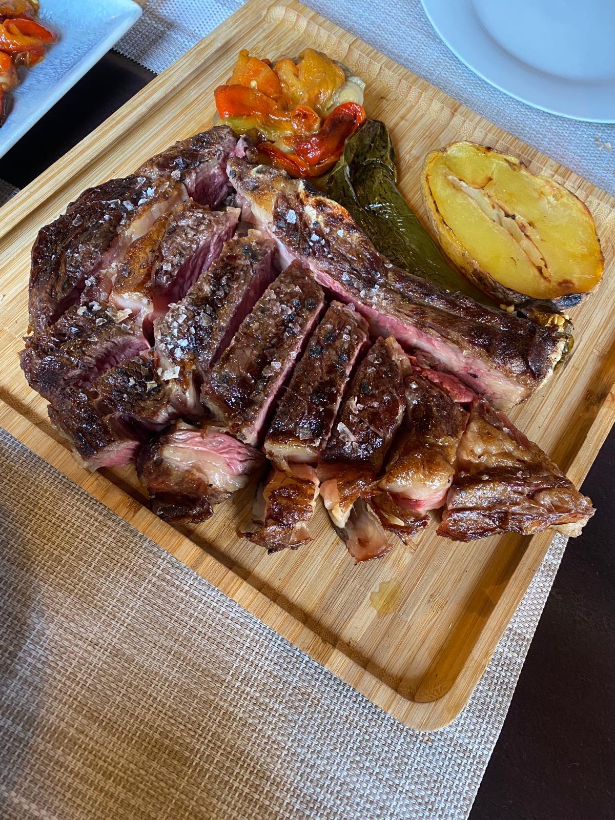 Entrecot a la brasa cortado, con pimientos escalivados y patata al horno, en tabla de madera