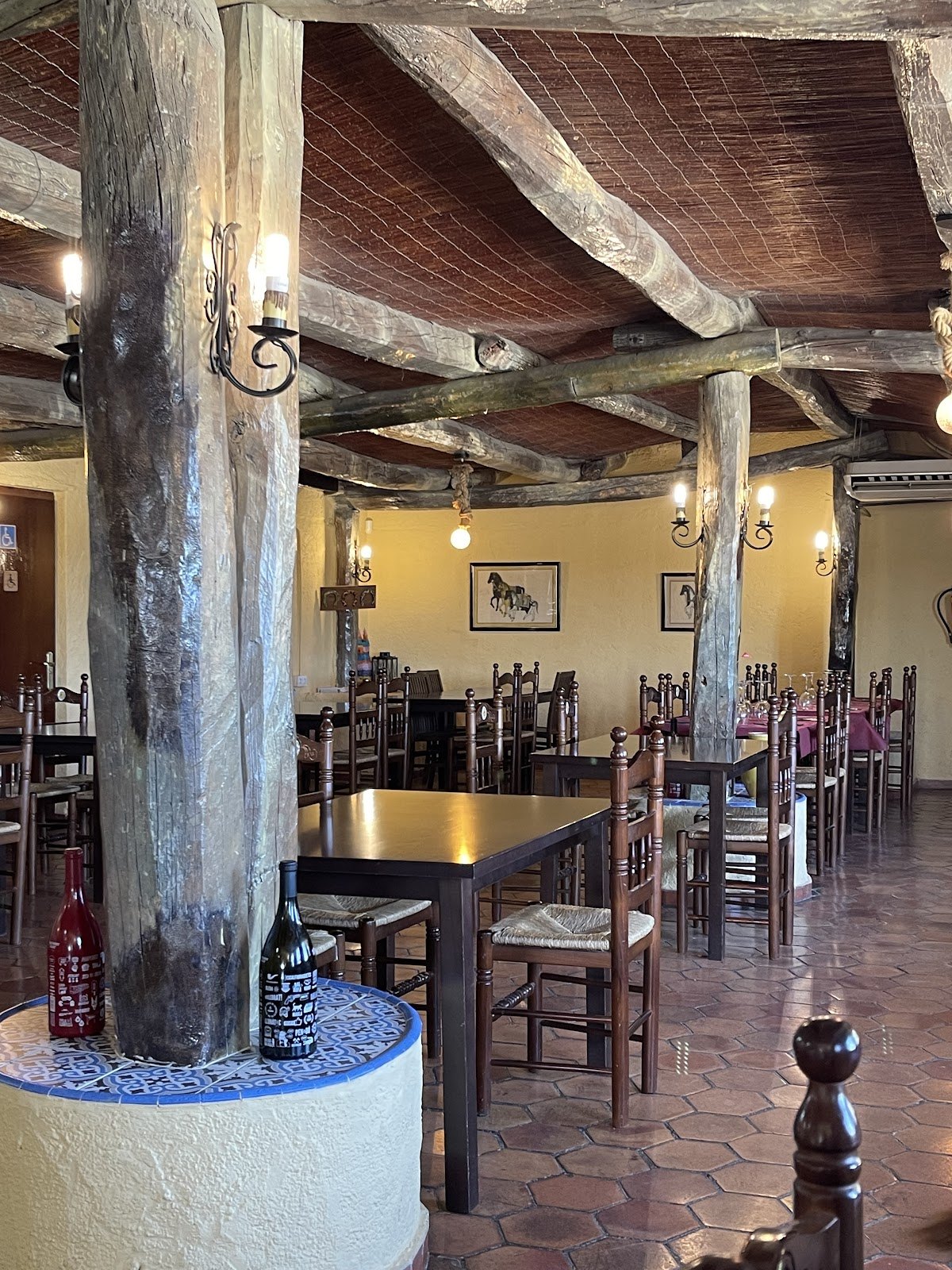 Comedor rústico de La Serreta con columnas de troncos, vigas y cuadros de caballos